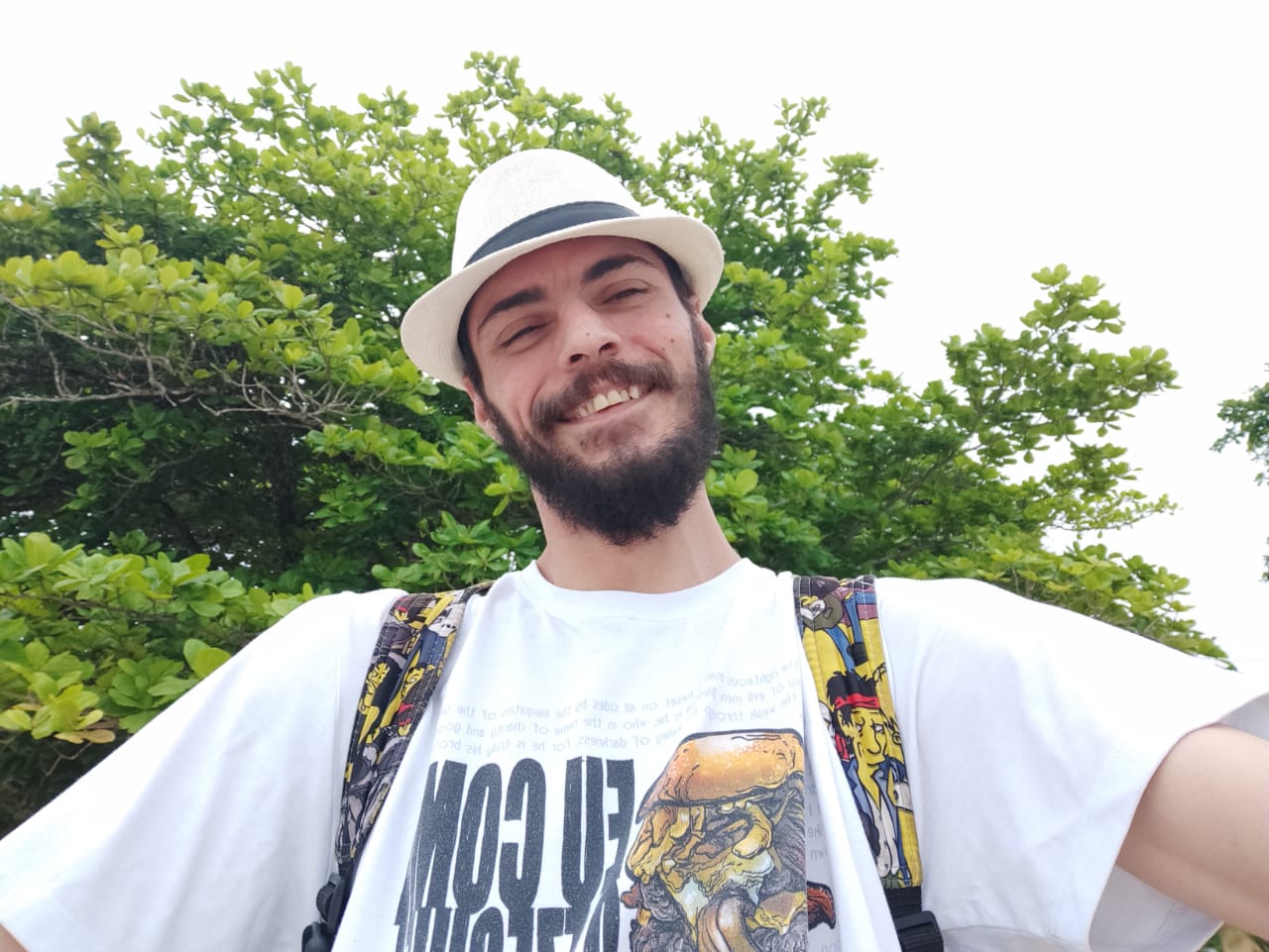 foto, homem branco, de chapéu e sorridente, com braços abertos e rodeado por árvores